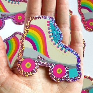 May include: A hand holding a white roller skate with rainbow stripes and pink glitter. The skate has turquoise wheels and pink accents.