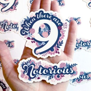 May include: A collection of stickers with floral designs and text. One sticker reads "When there are 9" with a large number 9. Another sticker says "Notorious". The stickers have a white background with blue, pink, and purple floral accents.