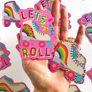 May include: Pink sticker with a rainbow roller skate and the text "Let's Roll" in glitter letters. The sticker is on a white background.