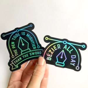 May include: Two black and iridescent holographic stickers with a pen and text. The first sticker says "The pen is mightier than the sword". The second sticker says "Bezier all day".