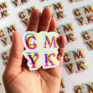 May include: A sticker with the letters CMYK in a rainbow color scheme. The letters are layered on top of each other, creating a 3D effect.