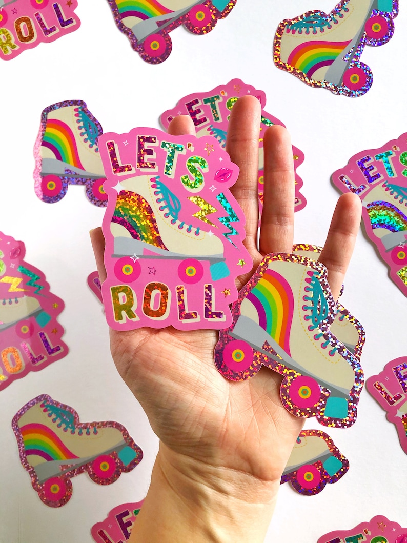 May include: Pink sticker with a rainbow roller skate and the text "Let's Roll" in glitter letters. The sticker is on a white background.