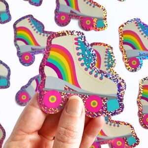 May include: A set of rainbow roller skate stickers with pink glitter. The stickers are in the shape of a roller skate with a rainbow design on the boot and pink wheels.