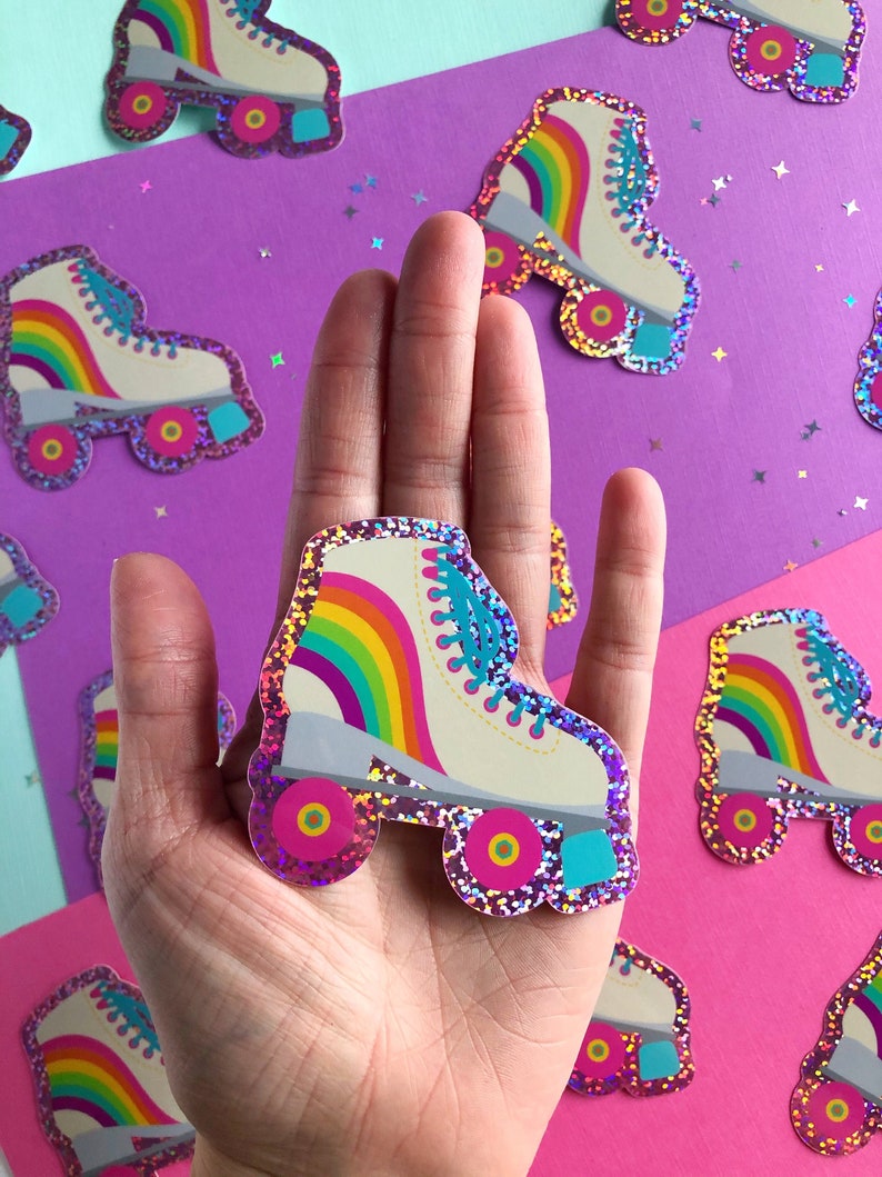 May include: A rainbow roller skate sticker with glitter. The sticker is white with a rainbow stripe and blue laces. The wheels are pink with a yellow center.