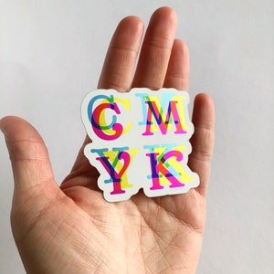 May include: A sticker with the letters CMYK in a layered, multi-colored design. The letters are outlined in black and filled with shades of cyan, magenta, yellow, and black.