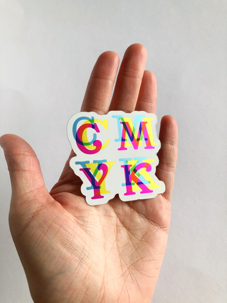 May include: A sticker with the letters CMYK in a layered, multi-colored design. The letters are outlined in black and filled with shades of cyan, magenta, yellow, and black.