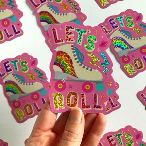 May include: Pink and white roller skate with rainbow glitter and the text "Let's Roll" in pink glitter.