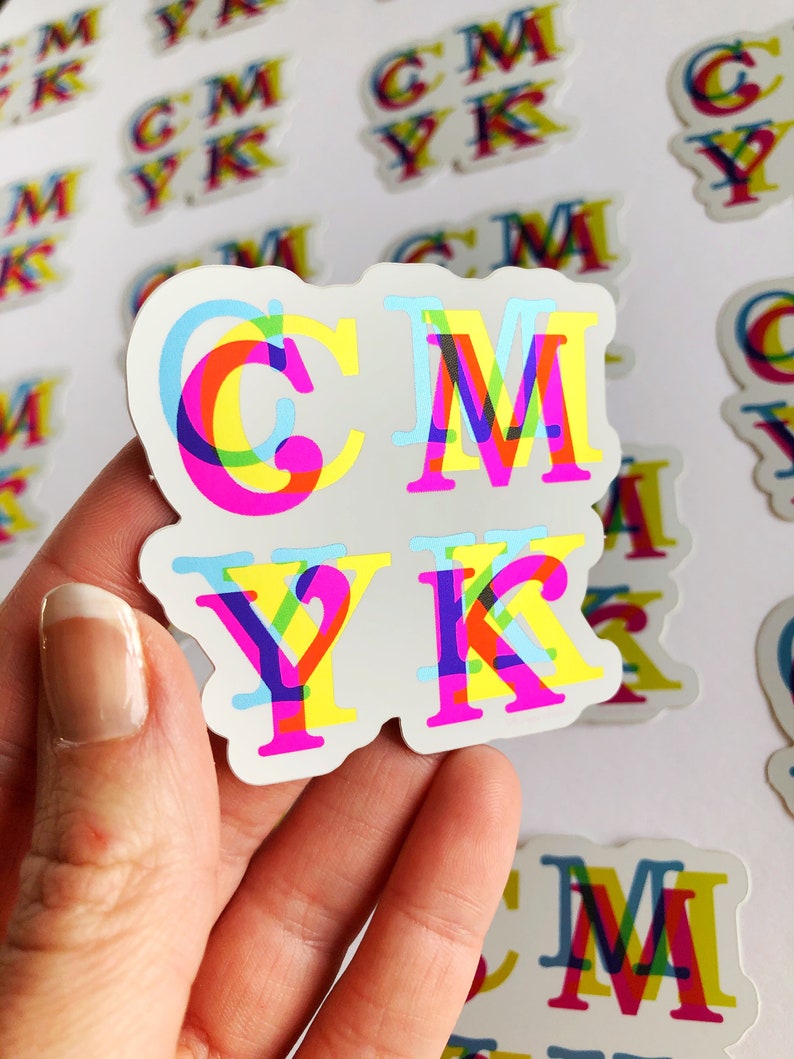 May include: A close-up of a sticker with the letters CMYK printed in a rainbow color scheme. The letters are layered on top of each other, creating a 3D effect.