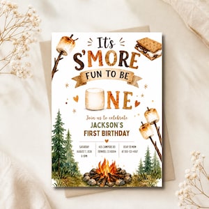 Op de afbeelding: Een witte verjaardagsuitnodigingskaart met aquarelillustraties van s'mores, een kampvuur en dennenbomen. De tekst luidt: It's S'MORE FUN TO BE ONE, Join us to celebrate JACKSON'S FIRST BIRTHDAY, Saturday August 7, 2026, 6-8PM, 435 Campfire Rd, Denver, CO 80004, RSVP to Mom at 555-123-4567.