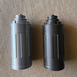 May include: Two cylindrical objects with a stepped, tiered top and vertical ribbed detailing along the sides. One object is finished in a smooth, metallic silver color, while the other is finished in a dark, matte charcoal gray color.