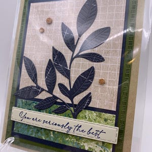 May include: Greeting card with a dark green embossed border and a central design featuring a dark gray leaf branch. The card includes the text "You are seriously the best" on a cream-colored banner.
