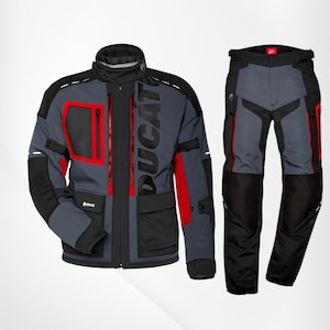 May include: A motorcycle jacket and matching trousers set in grey, black, and red. The jacket features a high collar, vertical zips, multiple pockets, and the word DUCATI printed vertically. The trousers have a grey and black colour-blocked design.
