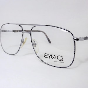 May include: Aviator-style eyeglasses with a grey and black speckled pattern on the metal frames. The clear lenses feature the black text eye Q ...the smart choice printed on the right side. The glasses include a double bridge and nose pads.
