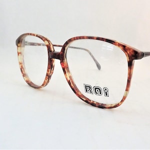 May include: Tortoiseshell-patterned eyeglasses with a brown and amber mottled frame. The lenses are clear, and the right lens features the text "RQi" printed in a bold, black, outlined font. The temples are thin and metallic in appearance.