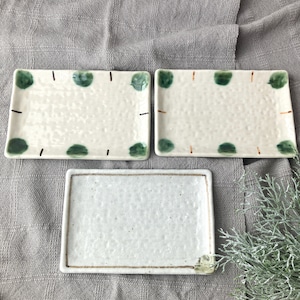 May include: Three rectangular ceramic plates. Two plates have a white background with green polka dots and brown dashes. The third plate is white with a brown border. The plates are arranged on a gray surface.