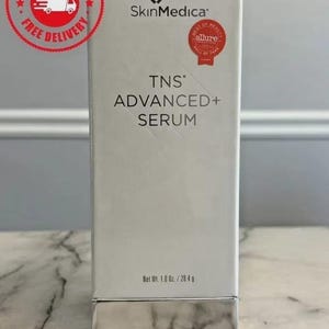 Op de afbeelding: Een witte SkinMedica TNS Advanced+ Serum doos met de tekst "TNS ADVANCED+ SERUM". De doos heeft een rode "Best of Beauty" sticker en een "Free Delivery" sticker. Netto gewicht: 28,4 g.