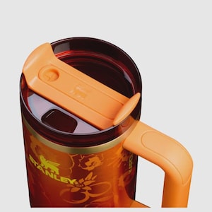 May include: A Stanley brand travel mug featuring a vibrant orange and red floral pattern on the exterior. The mug includes a translucent dark red lid with an orange sliding closure, a matching orange handle, and the Stanley logo printed in yellow.