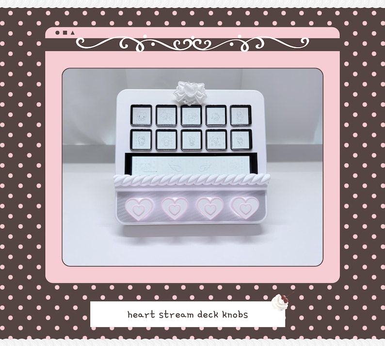 May include: A white stream deck console featuring ten square buttons with engraved icons, a central horizontal display screen, and four light pink heart-shaped knobs at the base. The device is topped with a small white bow-shaped decorative element.