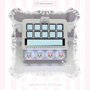 May include: A white custom macro pad featuring ten square buttons with line art icons, a long horizontal display screen, and four round knobs with cat faces in blue and pink. The device is adorned with a white bow and wing accents, labelled with the text @dollettedesigns and cutie.