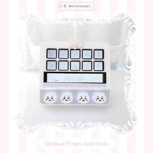 May include: A white custom stream deck featuring ten square buttons with light blue character illustrations, a horizontal display bar with wing graphics, and four circular knobs adorned with white cartoon faces and pink blush details.