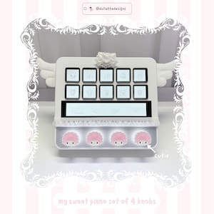 May include: A white rectangular console featuring a top row of ten square buttons with character illustrations, a central horizontal display, and a bottom row of four pink-haired character knobs labelled cutie. It includes a bow and wing accents.