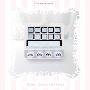 May include: A white stream deck featuring ten square buttons with light gray character illustrations, a horizontal display screen with wing graphics, and four circular knobs at the bottom decorated with white cartoon faces wearing glasses.