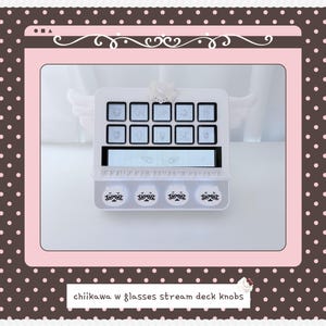 May include: A white stream deck controller featuring ten square buttons with character icons, a central display screen with wing graphics, and four circular knobs at the bottom decorated with cartoon faces wearing glasses. The text reads chiikawa w glasses stream deck knobs.