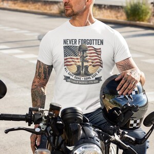 May include: White t-shirt with the text "NEVER FORGOTTEN" above an American flag and a soldier's memorial. The shirt also features the text "ALL GAVE SOME - SOME GAVE ALL" and "250 YEARS OF SACRIFICE - 1776-2026".