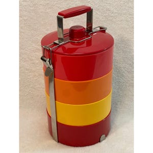 May include: A cylindrical four-tier food carrier featuring a stack of red, orange, and yellow containers. It includes a metal locking frame with a red handle on top, designed to secure the stacked compartments together for transport.