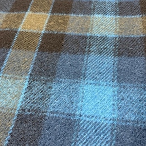 Pode incluir: Close-up de um tecido tecido com um padr&atilde;o xadrez. O design apresenta uma grade de linhas que se cruzam em tons de azul, marrom e bege. O tecido tem uma apar&ecirc;ncia texturizada, sugerindo l&atilde; ou material semelhante.