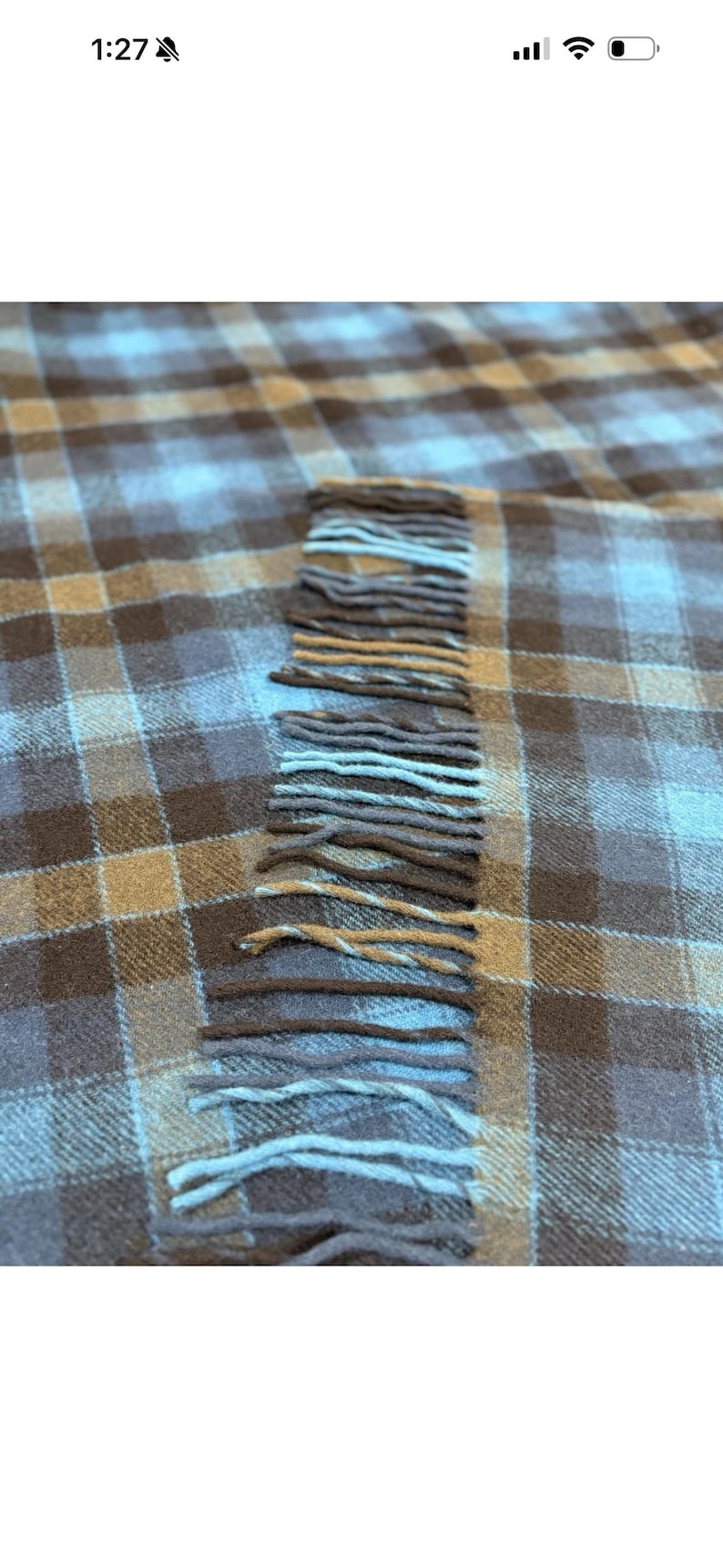 Pode incluir: Um close-up de um cobertor xadrez em tons de castanho, bege e azul. O cobertor tem uma borda com franjas com cores alternadas de castanho e azul. O cobertor &eacute; feito de um material macio.
