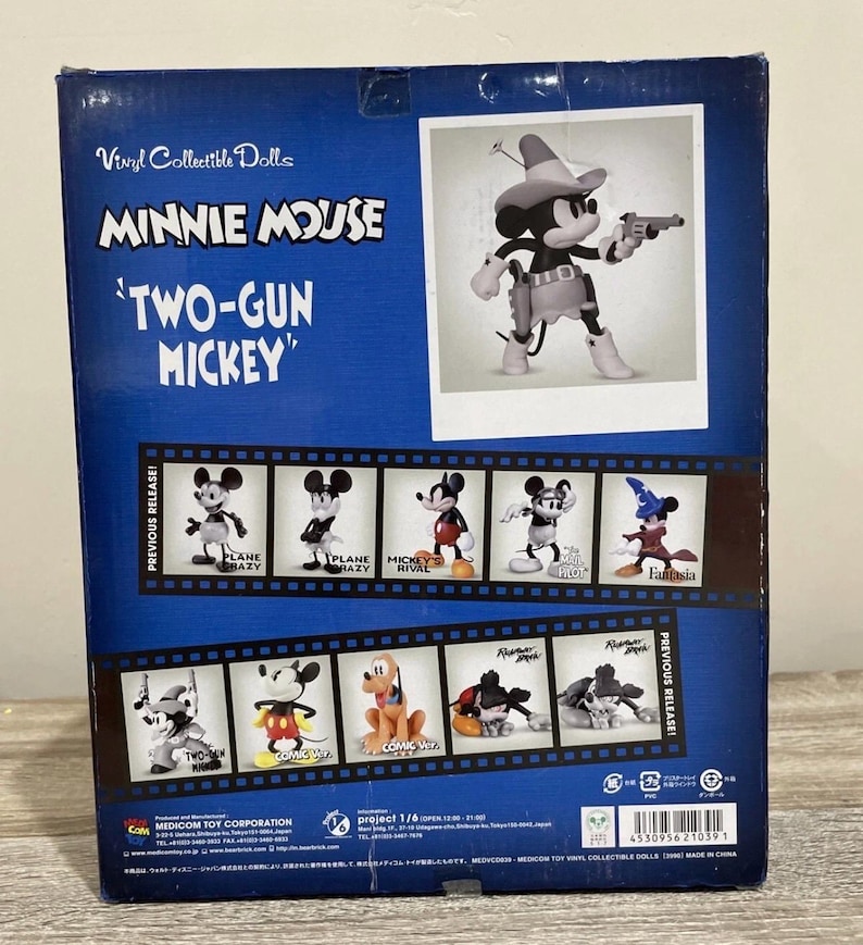 Pu&ograve; includere: Scatola blu per una bambola da collezione in vinile di Minnie Mouse, con "Two-Gun Mickey". La scatola include immagini di varie figure di Topolino e il testo "Vinyl Collectible Dolls".