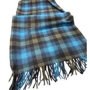 Pode incluir: Cachecol xadrez azul, preto e castanho com franjas. O cachecol &eacute; feito de um material macio e apresenta um padr&atilde;o xadrez cl&aacute;ssico. As franjas s&atilde;o de um tom azul mais escuro.
