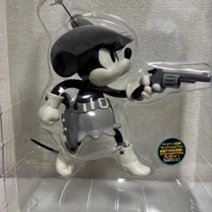 Pu&ograve; includere: Una statuetta nera, bianca e grigia di un topo dei cartoni animati in abito da cowgirl, con in mano un revolver grigio. Il topo indossa un cappello, una gonna e stivali. La statuetta &egrave; in una confezione di plastica trasparente.