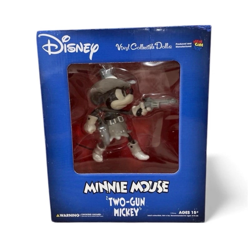 Pu&ograve; includere: Una bambola da collezione in vinile di Minnie Mouse in scatola. La bambola &egrave; vestita da cowgirl, con una pistola in mano. La scatola &egrave; blu con il logo Disney e il testo "Minnie Mouse 'Two-Gun Mickey'" e "Vinyl Collectible Dolls". Et&agrave; 15+.