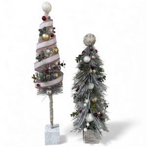 May include: Two decorative artificial Christmas trees with silver-toned needles. The taller tree features a spiraling white ribbon with red trim, gold and silver ornaments, and a white sphere topper. The shorter tree has silver and red baubles.