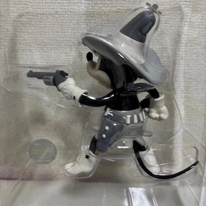 Pu&ograve; includere: Statuetta in bianco e nero di un topo dei cartoni animati in tenuta da cowboy, con una pistola. Il topo indossa un cappello da cowboy grigio, un gilet e stivali con una stella su ogni stivale. La statuetta &egrave; in una confezione di plastica trasparente.