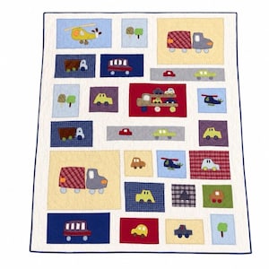 May include: A patchwork quilt with a white background and blue borders, featuring appliquéd vehicles like trucks, cars, and helicopters. The quilt is composed of colourful squares with different patterns and colours, creating a playful design for a child's room.