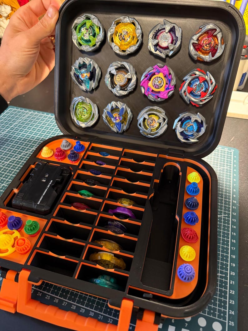 May include: A black and orange carrying case filled with colorful spinning tops. The case is open, revealing multiple compartments holding the tops and their accessories. The tops are various colors, including green, yellow, red, and blue.