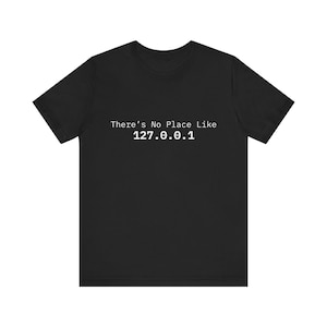 Könnte beinhalten: Schwarzes T-Shirt mit dem weißen Text "There's No Place Like 127.0.0.1". Das kurzärmelige Oberteil hat einen Rundhalsausschnitt. Der Text ist mittig auf der Brust platziert, geeignet für den Alltag.