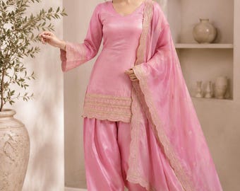 May include: A light pink three-piece outfit consisting of a V-neck tunic with long sleeves, matching loose-fitting trousers, and a sheer dupatta. The tunic and trousers feature gold embroidered scalloped borders, and the Leverice logo is visible.