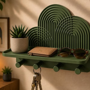 May include: A dark olive green wall-mounted shelf featuring a decorative arched back panel with concentric lines. The shelf includes four cylindrical hooks underneath, holding a set of keys, a small potted succulent, a brown wallet, and sunglasses.