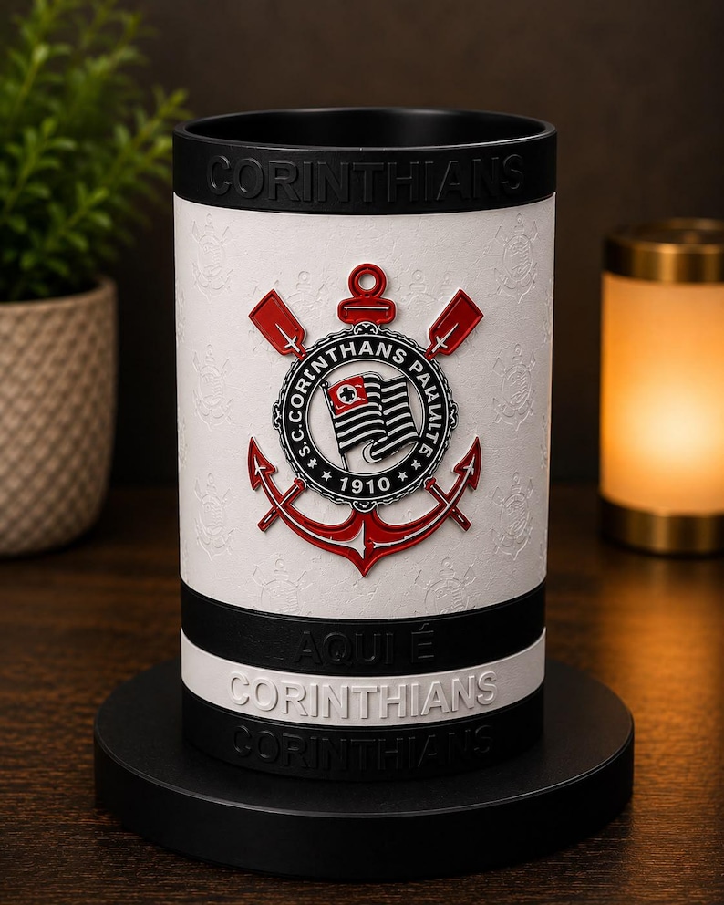 May include: A white and black Corinthians-themed tumbler. The tumbler displays the Corinthians emblem in red and white, with the text "CORINTHIANS" and "AQUI &Eacute; CORINTHIANS" in white. The tumbler is set on a black base.