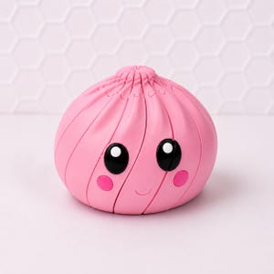 May include: A round, pink, dumpling-shaped object with a pleated top. It features two large, glossy black eyes with white highlights, two small pink circular cheeks, and a thin, curved line representing a smiling mouth on the front surface.