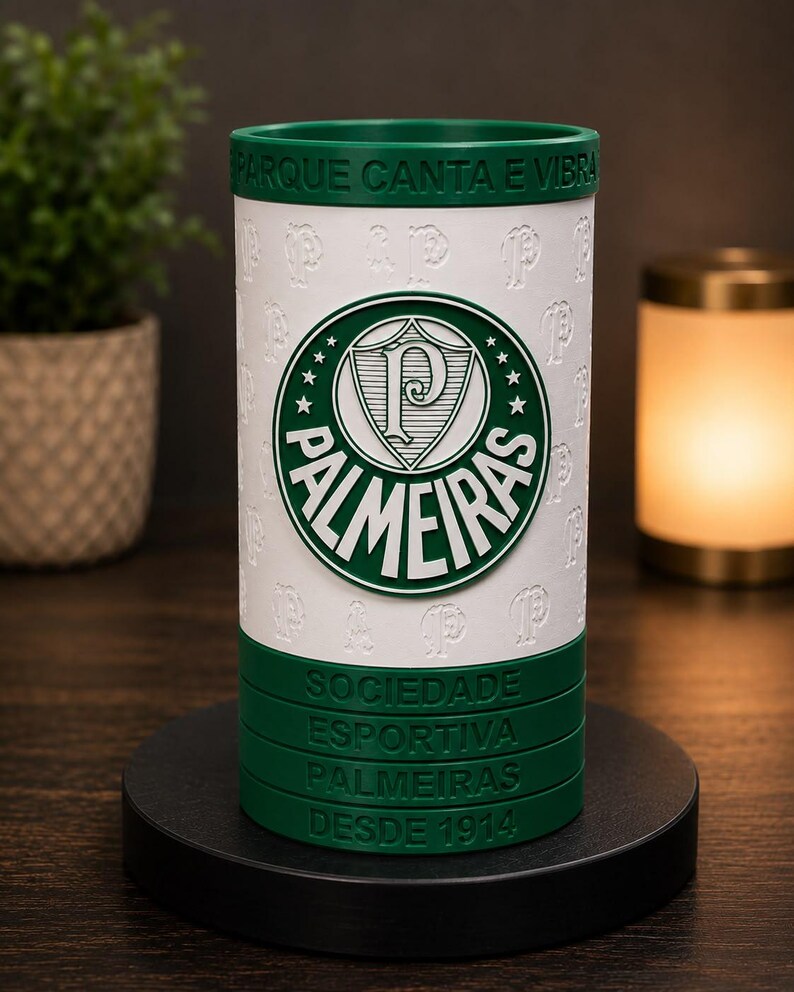 May include: A white and green cylindrical tumbler with the Palmeiras logo. The design includes the team's emblem, the words "PARQUE CANTA E VIBRA", and "SOCIEDADE ESPORTIVA PALMEIRAS DESDE 1914". The tumbler is on a black base.