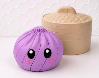 May include: A purple dumpling-shaped object with a smiling face, large black eyes, and pink cheeks, positioned in front of a beige, cylindrical, lidded container with a textured, woven-style pattern on the lid and smooth sides.