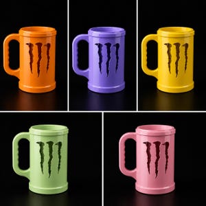 Puede incluir: Un conjunto de cinco tazas cil&iacute;ndricas en naranja, morado, amarillo, verde claro y rosa. Cada taza presenta un recorte prominente del logotipo de Monster Energy en el frente e incluye un asa lateral resistente con agarre texturizado.