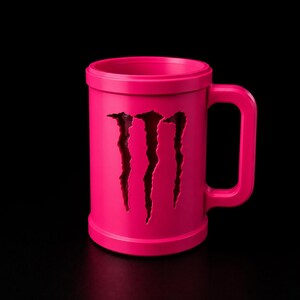 Puede incluir: Una taza de color rosa brillante que presenta un dise&ntilde;o recortado de tres marcas de garras verticales en la parte frontal. La taza tiene un cuerpo cil&iacute;ndrico con un borde grueso y un asa rectangular resistente en el lateral.