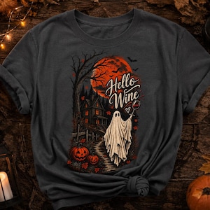 Könnte beinhalten: Ein dunkelgraues T-Shirt mit einem Grafikdruck eines weißen Geistes, der ein Weinglas hält. Die Szene zeigt ein Spukhaus, einen großen orangefarbenen Mond, kahle Bäume und Kürbisse. Der Text "Hello Wine" steht in einer Schreibschrift über dem Geist.