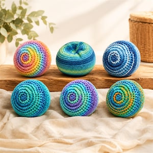 Puede incluir: Seis bolas de ganchillo coloridas en varios tonos de azul, verde, morado, amarillo y naranja. Las bolas tienen un diseño en espiral y están dispuestas sobre una superficie de madera y una tela color crema.